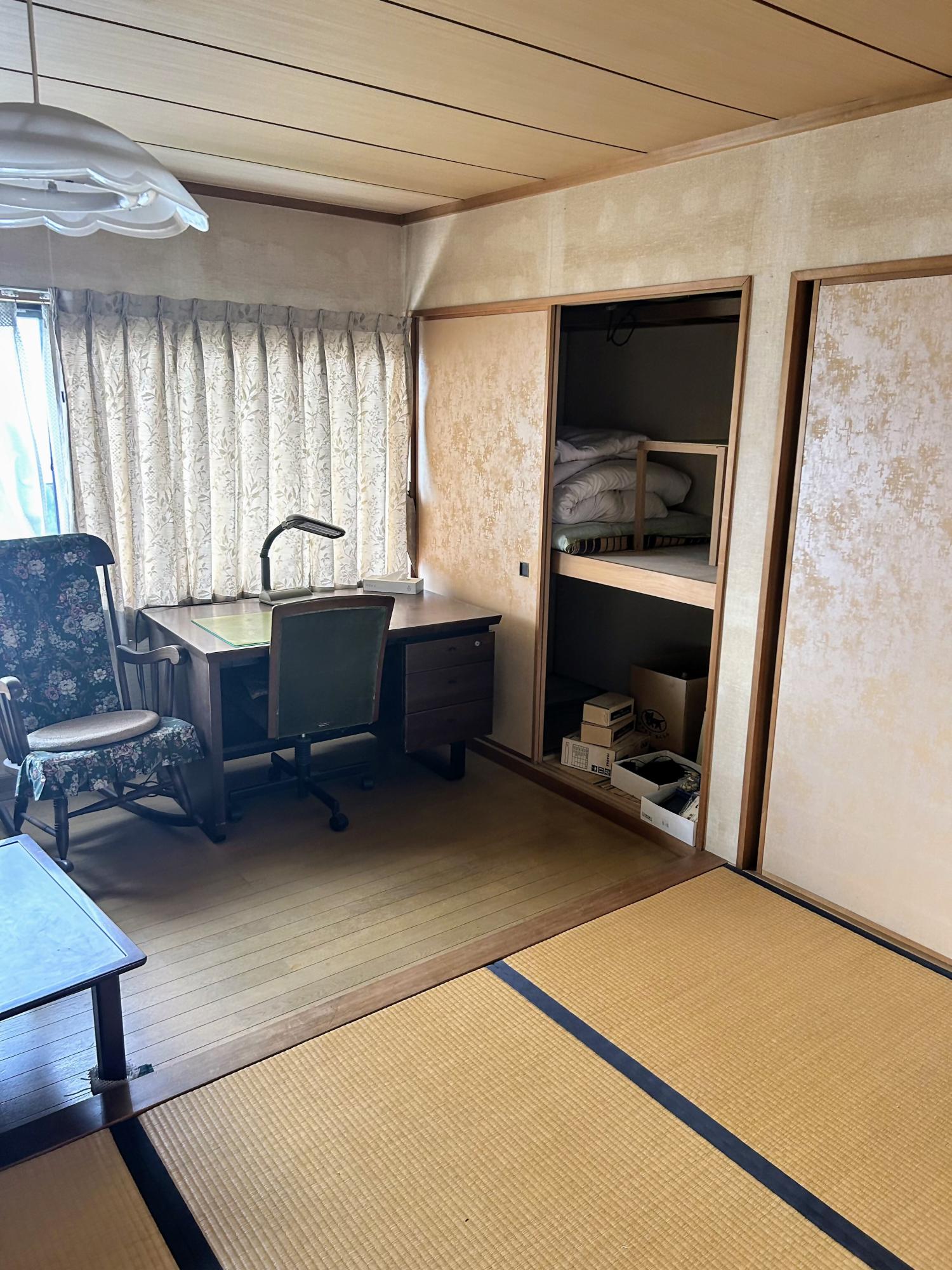 畳敷きの和室に机や椅子が置かれ、押し入れには寝具や収納物が収められた生活感のある室内の写真
