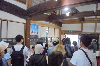 サガ電子工業株式会社の社屋内で、小柳社長の説明に耳を傾ける参加者の様子。