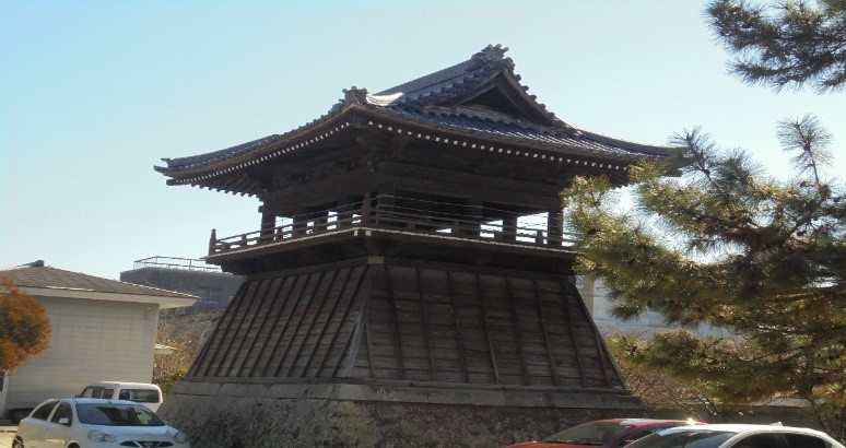 石垣の上に建つ木造の鐘楼が青空の下で堂々と佇む願正寺の写真