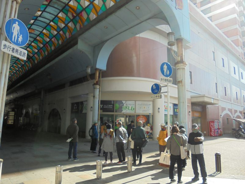 色鮮やかな天井が続く商店街の入口付近で人々が店先に集まり立ち話をしている様子を写した写真