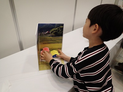 作り終わったジオラマを、棚田の写真の背景素材に組み合わせて、背景と色が合っているか確認する子どもの様子