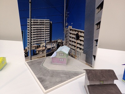 子どもが作ったジオラマを、ビル群の写真を用いた背景素材に組み合わせて飾っている様子