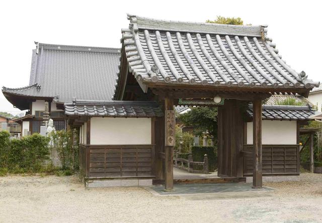 重厚な本瓦葺きの屋根を持つ伝統的な山門が手前に建ち、その奥に大きな瓦屋根の本堂が佇む、歴史ある寺院の静かな境内の風景を捉えた写真