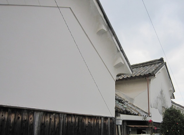 建物の最上部が鋭角に尖った「切妻造（きりづまづくり）」の白壁が連なり、腰壁部分の黒い板張りと鮮やかな対比をなす、歴史ある蔵や家屋の力強い造形を見上げるように捉えた写真