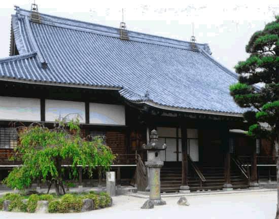 瓦屋根と木造の構造が特徴的な日本の伝統的寺院で、正面に広い階段と縁側があり、庭には石灯籠や植木が配置された願正寺の写真