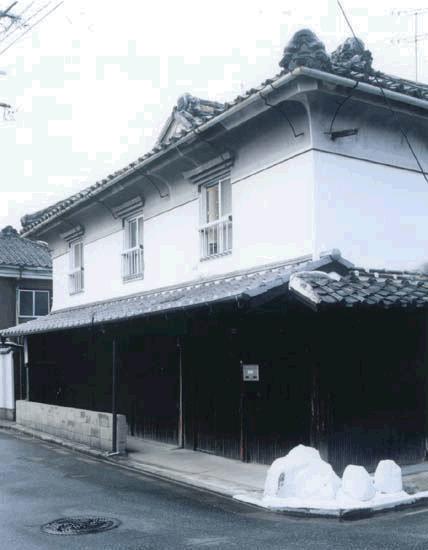 白壁と瓦屋根を持つ日本の伝統的な町家風建物で、二階に格子窓が並び、黒い板壁と低い塀が道路沿いに続く山下邸の外観写真