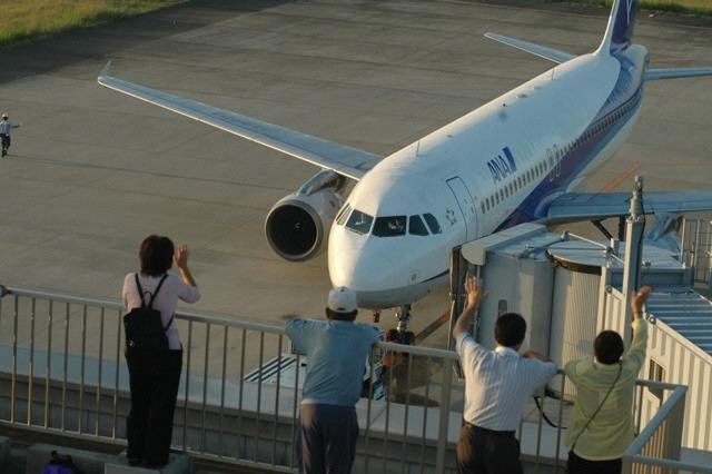 展望デッキの来訪者がタラップに接続された旅客機に向かって手を振り見送る様子を捉えた写真
