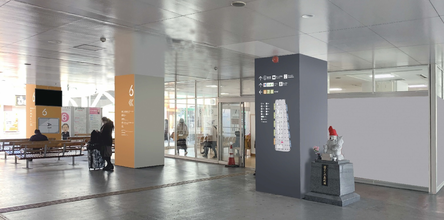 屋外通路にオレンジと灰色の案内柱が立ち並び、休憩用ベンチや小さな石像が配置された駅前空間を写した写真