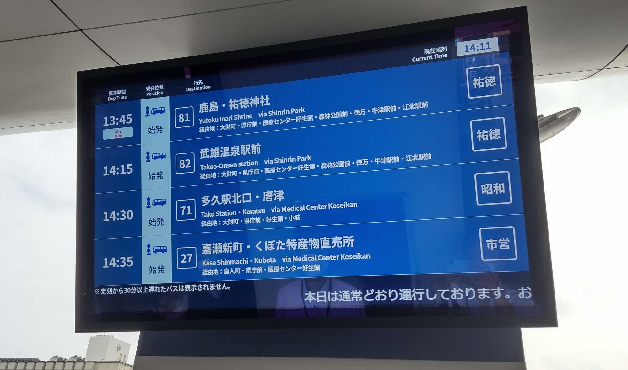 青い背景に複数路線の発車時刻や行き先が一覧表示されたバス案内モニターを捉えた写真