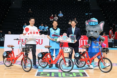 バスケットコート上で赤いシェア自転車と関係者、チームマスコットが並びPRを行う様子を写した写真
