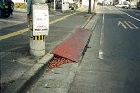電柱の脇の歩道から車道にかけて、段差を解消するために設置された赤茶色の鉄板が斜めに置かれている写真
