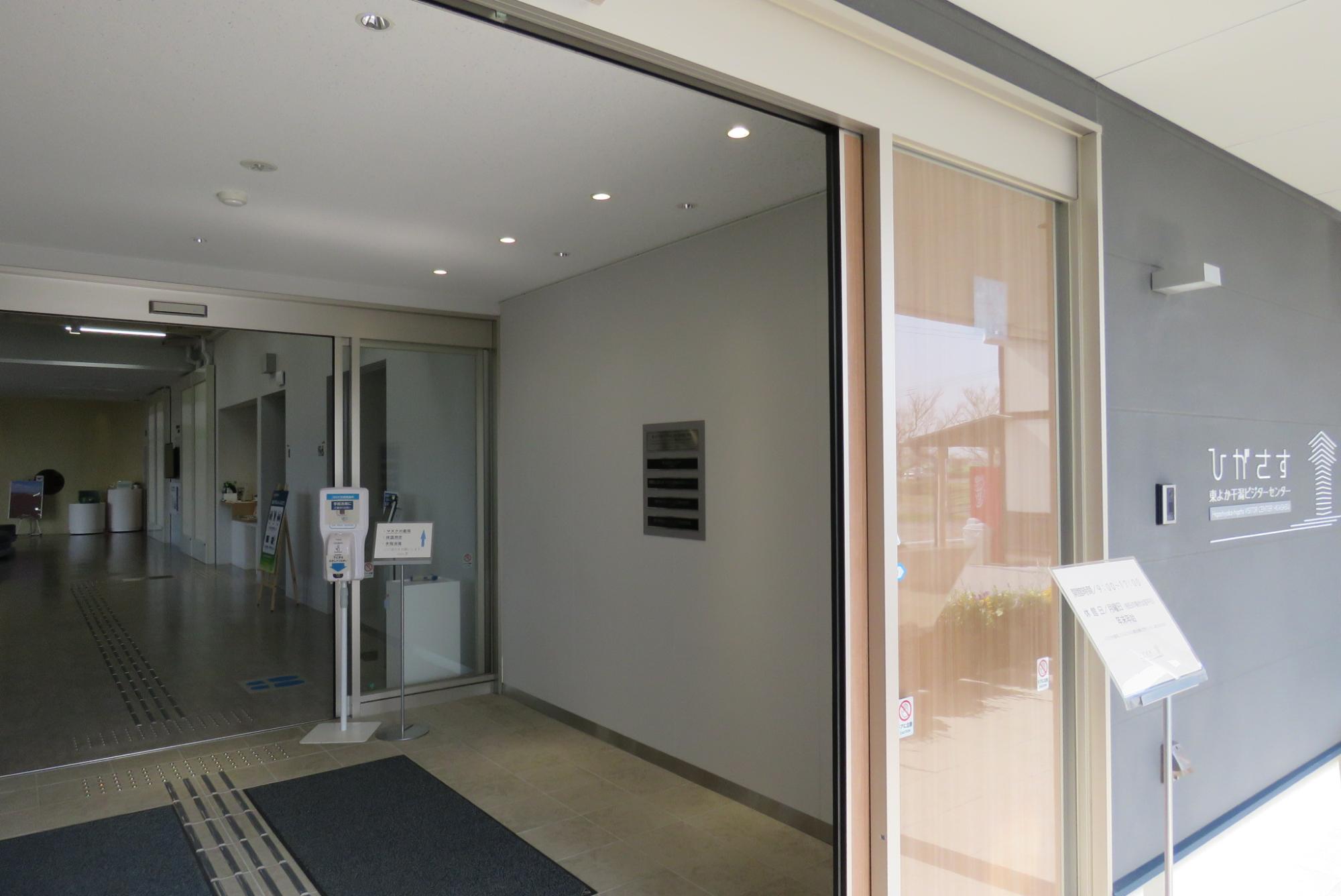 ひがさすのロゴが壁面に掲示されたガラス張りの自動ドア付きエントランスホールに銘板が設置されている写真