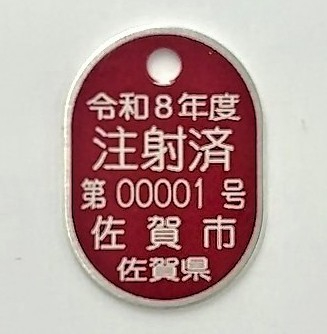 赤い楕円形のプレートに「令和8年度 注射済 第00001号 佐賀市 佐賀県」と白文字で刻印された注射済票