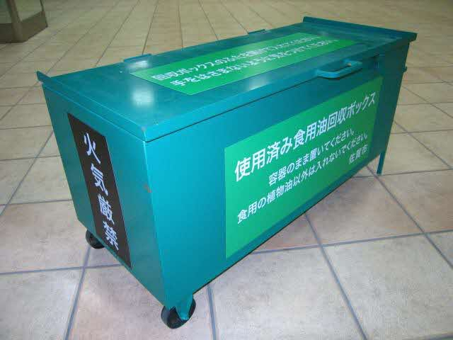 タイル敷きの床に置かれた、キャスター付きの緑色の大きな金属製「使用済み食用油回収ボックス」を斜めから撮影した写真