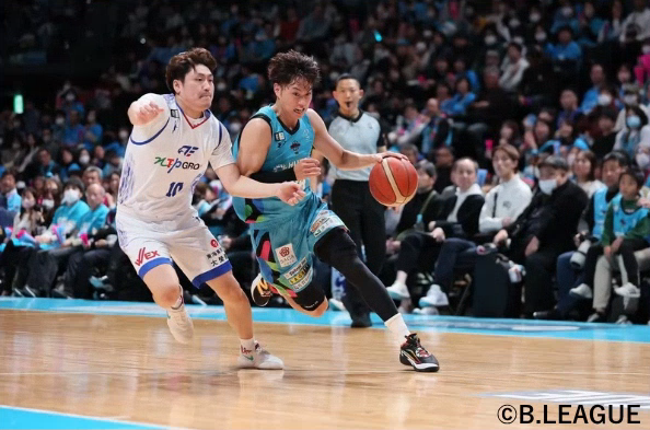 大勢の観客が見守る試合会場にて、水色のユニフォームを着た井上選手が相手ディフェンダーのマークを交わしながら力強くドリブルで切り込んでいく試合中の白熱したワンシーンを捉えた躍動感あふれる写真