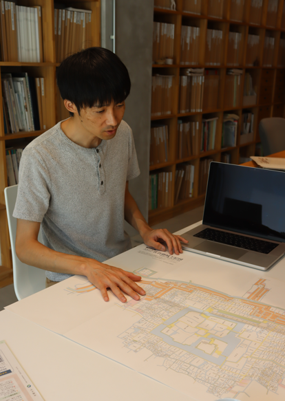 川崎さんが地図を広げた机の前に座り、作業をしている様子を写した写真