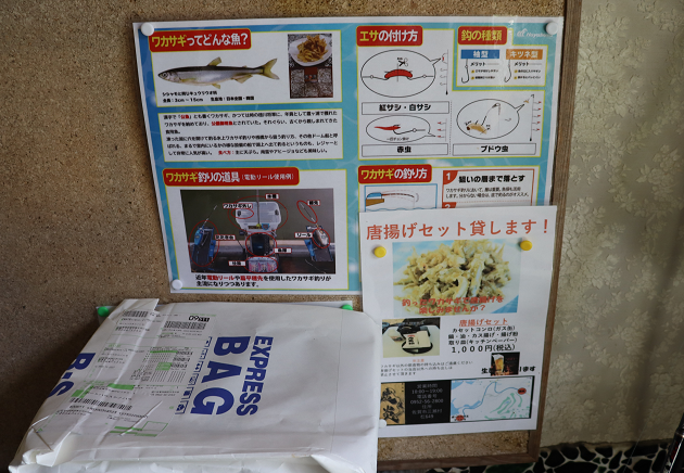 コルクボードに、ワカサギの生態や釣り方、道具の解説が写真やイラストと共に詳しく記載された案内板が掲示されており、その下には「唐揚げセット貸します！」という宣伝チラシが添えられた、釣り場のサービスを案内する写真