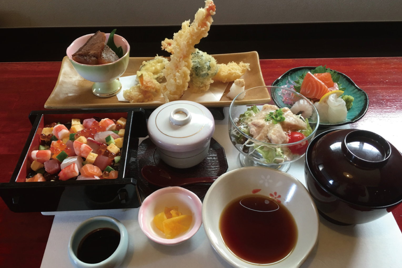 マグロやサーモン、海老、玉子などが色鮮やかに盛り付けられたバラちらし寿司を中心に、天ぷらの盛り合わせや刺身、茶碗蒸し、お吸い物などが並ぶ、桃の節句を祝う華やかで豪華なひなまつり御膳の写真
