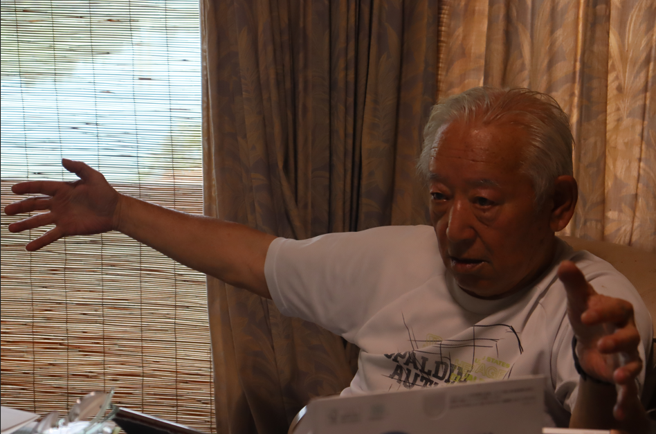 何かの大きさを表すように両腕を左右に大きく広げながら真剣な表情で熱心に話をしている篠原さんの写真