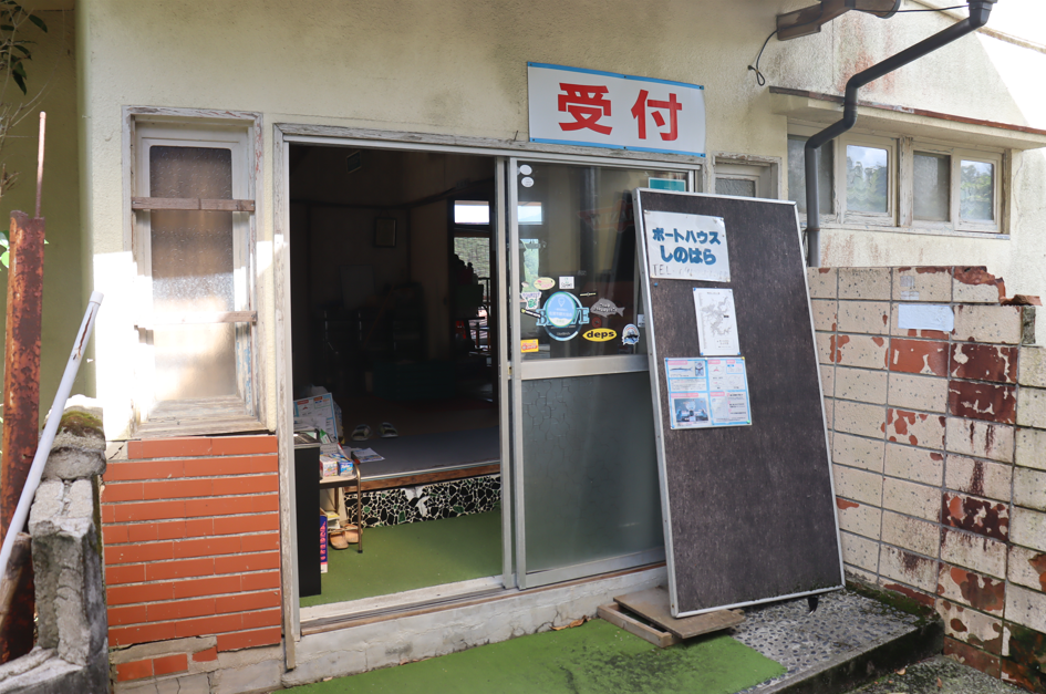 建物の入り口に赤字で「受付」と書かれた看板が掲げられ、引き戸の脇には「ボートハウスしのはら」と記された黒いボードが置かれている玄関前の写真