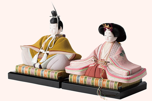 落ち着いた色合いの着物をまとったお内裏様とお雛様が、色鮮やかな菱形文様の畳台の上に並んで座り、日本の伝統的な美意識を感じさせる精巧な作りと穏やかな表情が印象的な、白背景に浮かび上がる美しい一対の雛人形の写真