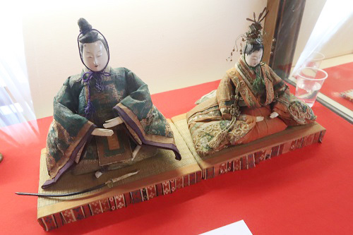 緑を基調とした落ち着いた色合いの着物を纏い、畳の台座に座る内裏雛が、赤い毛氈の上に仲良く並べられて展示されている、江戸時代に作られた歴史を感じさせる精巧な雛人形の写真