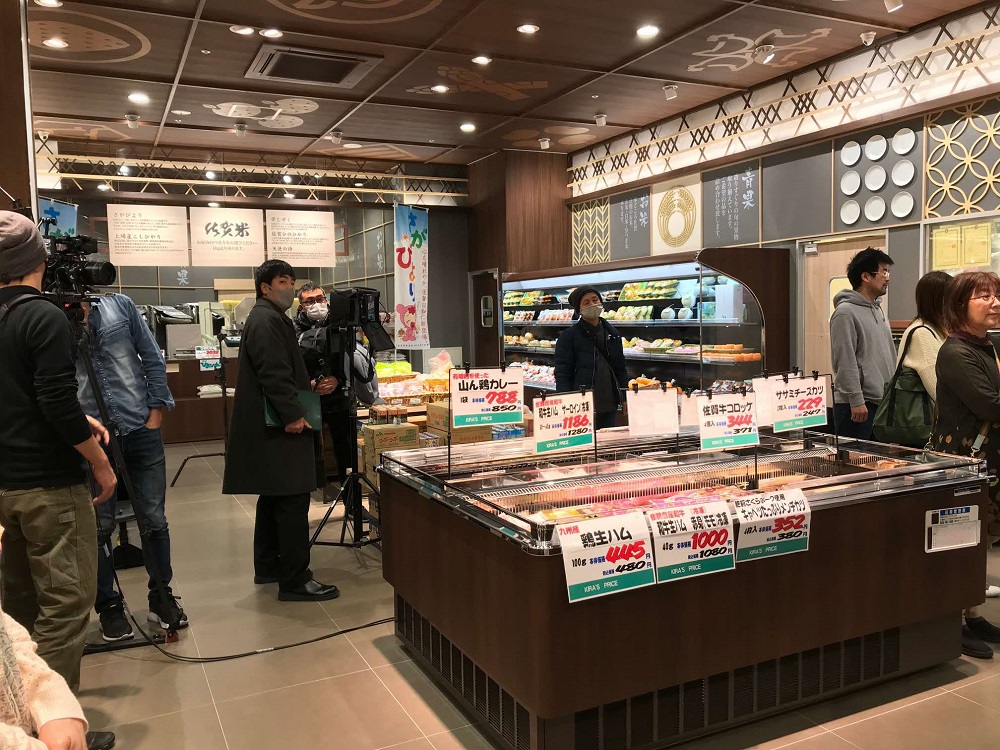 価格ポップがついた冷凍ショーケースが手前にあるスーパーマーケットの精肉売り場でテレビ番組の撮影クルーが複数のカメラを回して撮影している様子の写真
