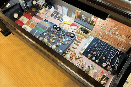畳敷きの店内に置かれたショーケースの中に、色鮮やかな佐賀錦の生地を用いた財布やストラップ、ペンダント、イヤリングなどの多彩な和装小物が整然と陳列されている写真