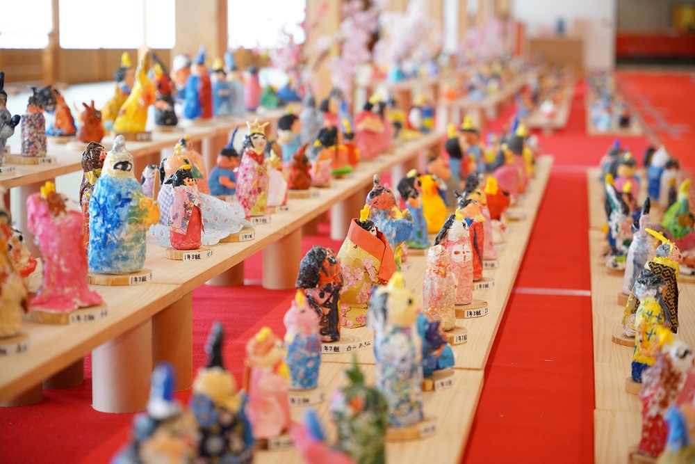 赤い絨毯が敷かれた広い室内に、木製の長い展示台が何列にも渡って並び、その上に色とりどりの紙や布で手作りされた個性豊かな雛人形たちが、奥まで途切れることなく整然と展示されている写真