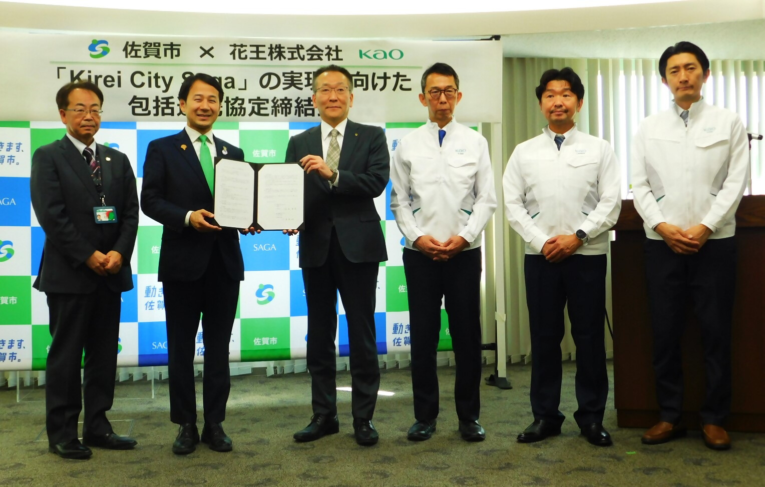 佐賀市と企業の協定締結式で複数の参加者が横一列に並び中央の二人が協定書を掲げて立つ写真