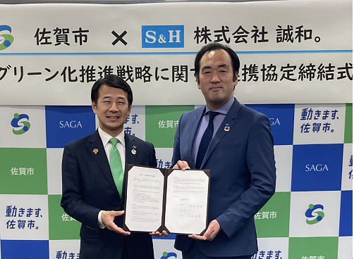 「佐賀市&times;株式会社誠和。グリーン化推進戦略に関する連携協定締結式」という看板を背に、坂井英隆佐賀市長と株式会社誠和 大出 浩睦代表取締役が協定書を手に持ち記念撮影をしている写真
