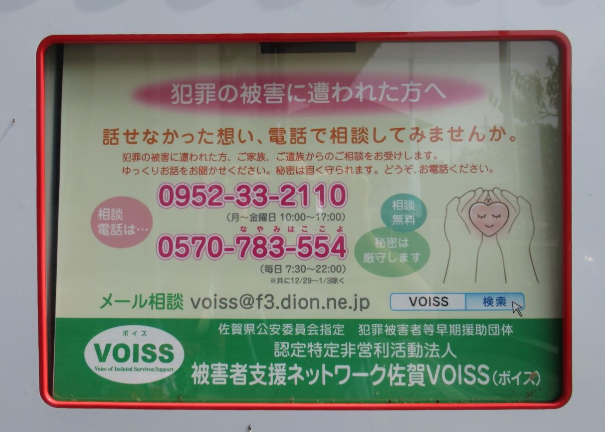 自動販売機の商品取り出し口の上に、犯罪被害に遭われた方への相談案内で、電話番号やメールアドレス、相談無料や秘密厳守の記載、緑色のVOISSロゴと検索ボタンが表示された案内板の写真