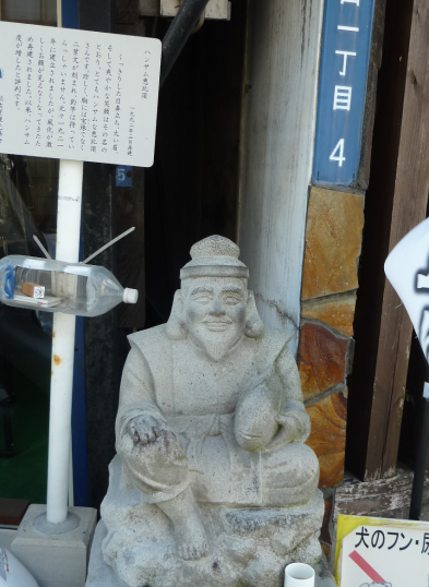 説明板や吊り下げられたペットボトルの横に座っているハンサム恵比須の写真