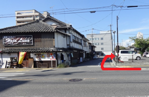 古い街並みに面した交差点越しの道路風景で、赤い矢印が歩道沿いに右方向への進行を明確に示している写真