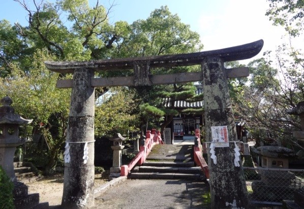 苔むした石造りの鳥居の奥に赤い橋と参道が続き、緑豊かな木々に囲まれた社殿が静かに佇む写真