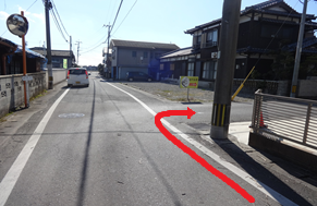 抜けるような青空が広がる冬の日、住宅が立ち並ぶ静かな細い道路において、電柱の脇から右側の路地へと曲がる進路を強調するように、路面に沿って大きな赤い矢印が合成されている、ルート案内用の風景写真