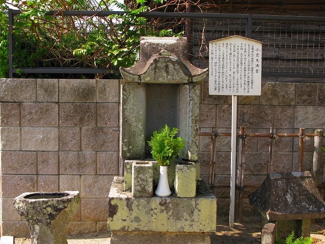 石造りの小さな祠の前に青々とした榊が白い花瓶に供えられ、傍らには「小児天満宮」の由緒が記された白い案内看板が立てられた、歴史を感じさせる静かな佇まいの史跡を捉えた写真