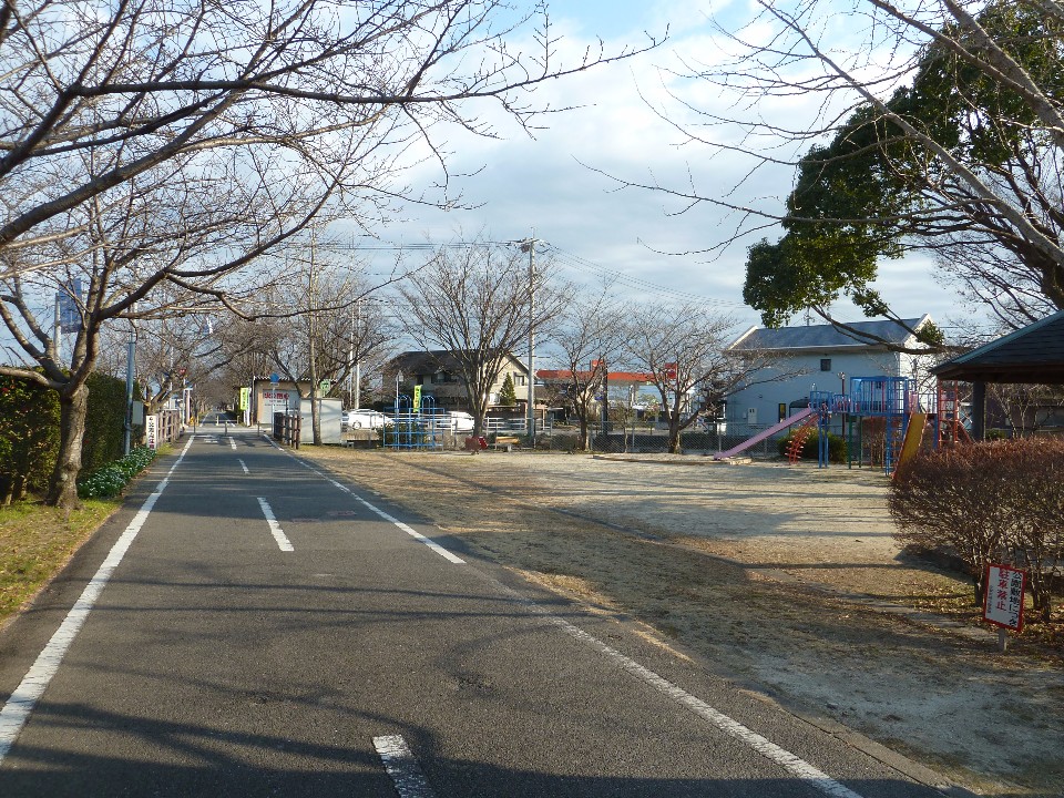 真っ直ぐな舗装路の右手に、滑り台やジャングルジムなどの遊具がある光法児童遊園の写真