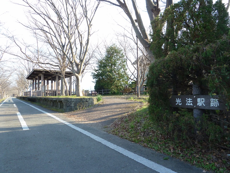 サイクリングロードに沿ってかつての駅のホームを思わせる石積みの土台と東屋が整備された手前右側に「光法駅跡」と記された木製の案内板が立っている写真