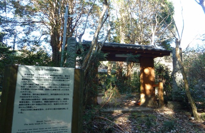 手前に設置された松陰寺の由来を説明する白い解説看板越しに、木々に囲まれ木漏れ日が差し込む厳かな雰囲気の山門を捉えた、佐賀市のウォーキングコース外にある史跡の情景を伝える写真