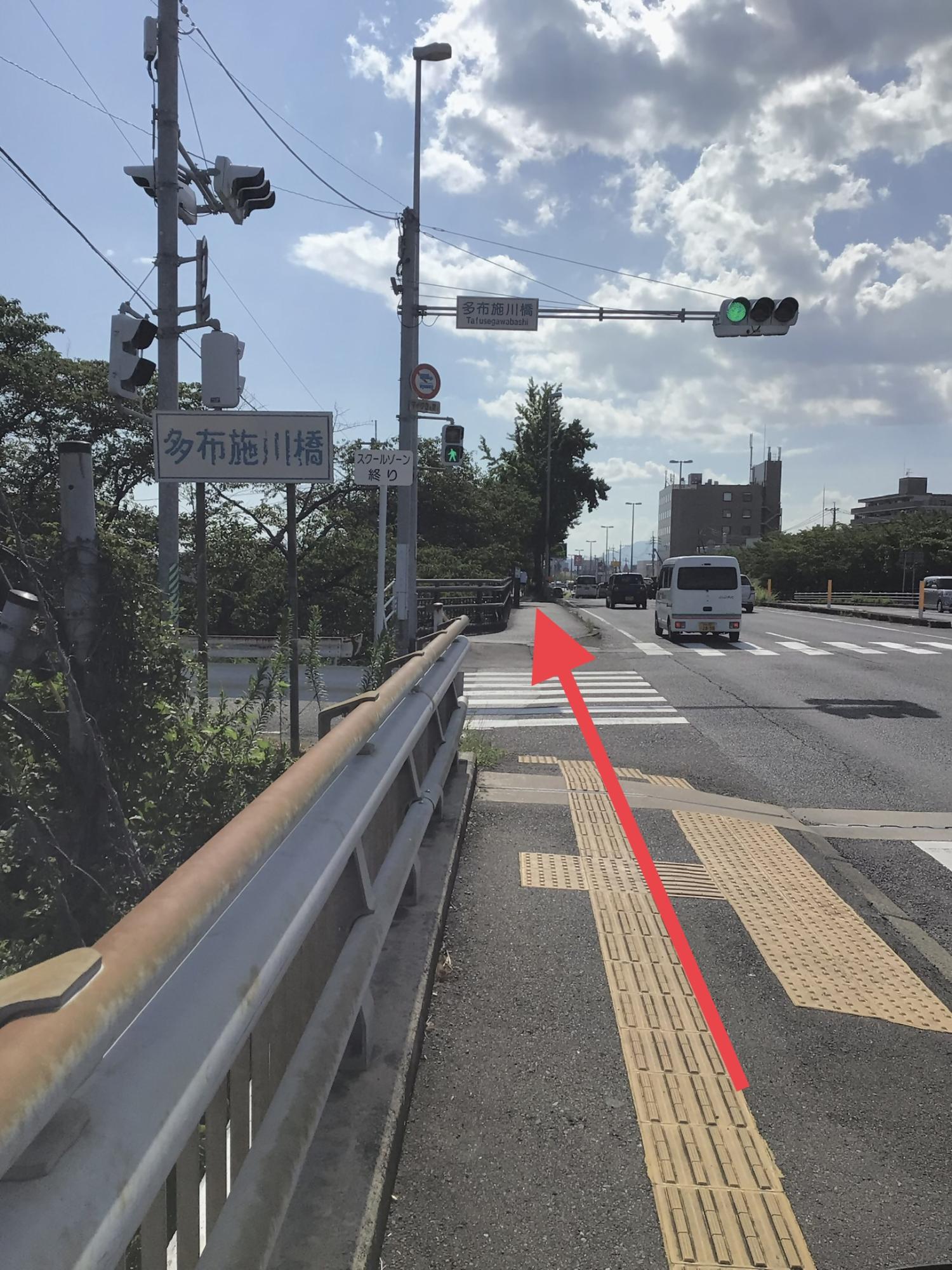 「多布施川橋」と記された大きな看板の脇を通り、青信号の交差点を渡って真っ直ぐに伸びる歩道を進むよう赤い矢印で示された、交通量の多い道路沿いの風景を捉えた写真
