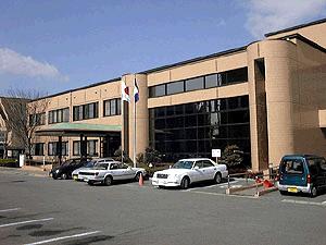 駐車場に面して建っているベージュ色の外壁と大きな黒いガラス窓を備えた二階建てのメートプラザ佐賀の外観写真