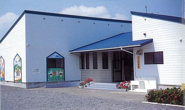 白い外壁と青い屋根の平屋建て施設が広い前庭と花壇に囲まれ、壁面の童話風イラストが明るい雰囲気を添えている久保田児童センター建物外観の写真