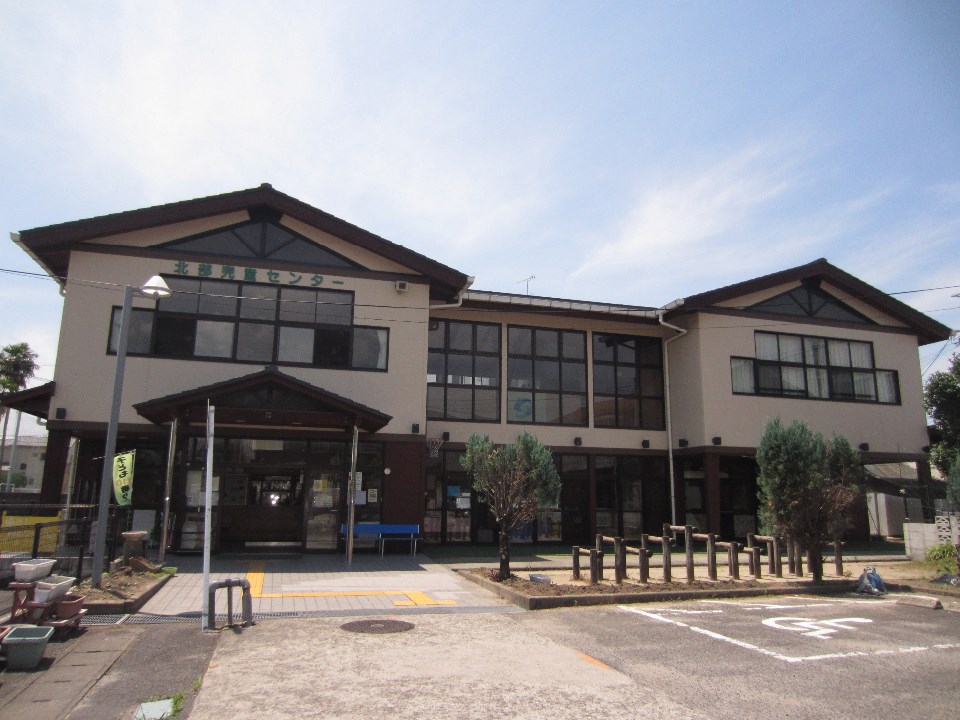 木造風の外観と大きな窓を備えた二階建ての北部児童センターが正面に広がり、周囲に駐車区画や植栽が整えられた写真