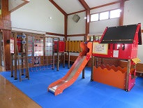 室内に鮮やかな赤い滑り台付き遊具とロープ遊具が青いマット上に並んで設置された写真