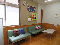 明るい室内に緑色のソファと色とりどりのクッションが並び、壁に子ども向けの装飾が掲示された落ち着いた授乳室の写真