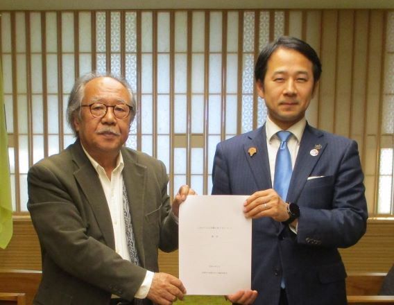 和室風の室内で五十嵐勉委員長と市長が並んで書類を正面に掲げ、提出完了を示す姿を収めた写真