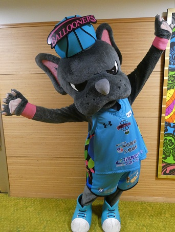 青いユニフォーム姿のマスコット「バルたん」が両腕を大きく広げてポーズをとる室内での様子を捉えた写真