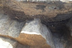 街道の整地面と土塁の境界付近に掘られ、現在は茶褐色の土に覆われた、雨水などを排水するために設けられたと考えられる細長い遺構の断面を捉えた写真。