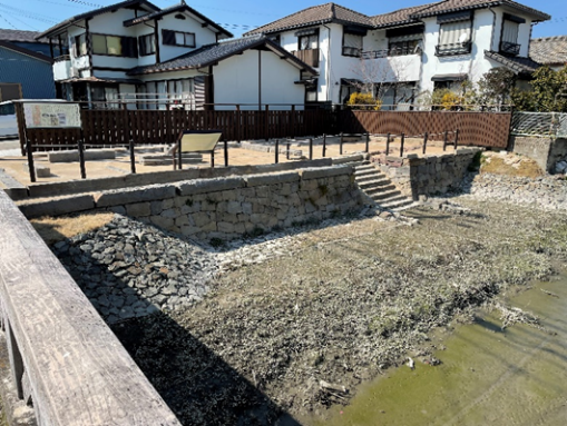 堅牢な石垣の上に組まれた平坦な広場から石段が下層の湿地帯へと続き、周囲には案内板や転落防止用の柵が整備された、歴史的な遺構の写真